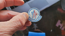 Cargar imagen en el visor de la galería, Hand holding a Moncler logo close-up with a blurred background